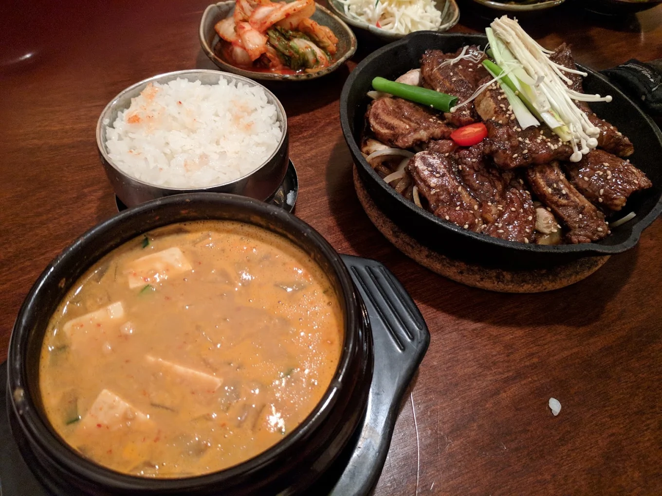 Chungok Jang fermented soybean stew in a stone pot beside LA galbi grilled short ribs, with rice and kimchi