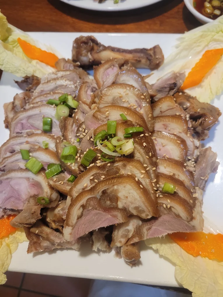 Sliced jokbal braised pork trotter fanned across a platter with scallion, sesame seeds and napa cabbage