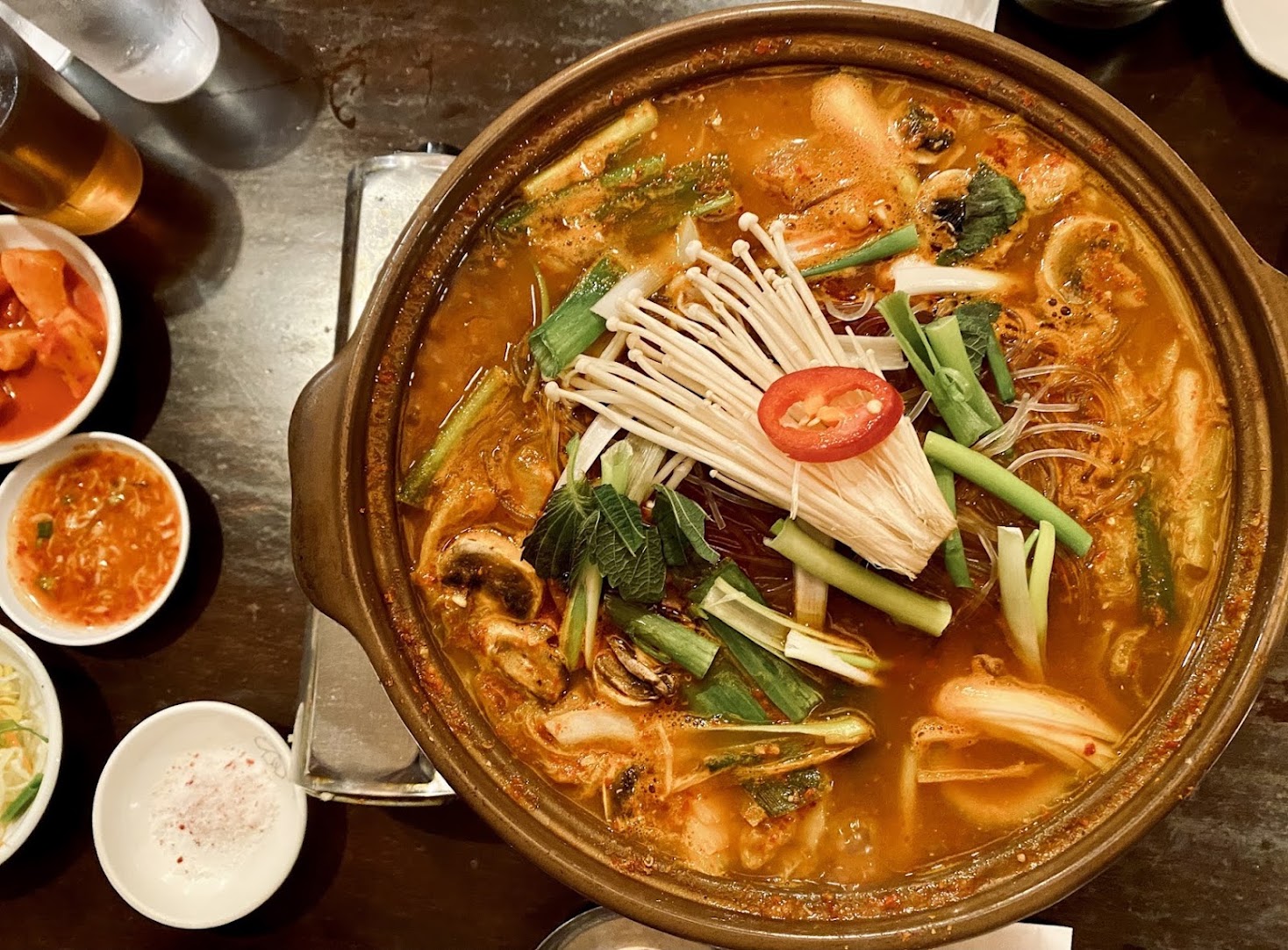 Pork neck bone stew (gamjatang) bubbling in a clay pot, topped with enoki mushrooms, scallions and perilla leaves, with banchan alongside