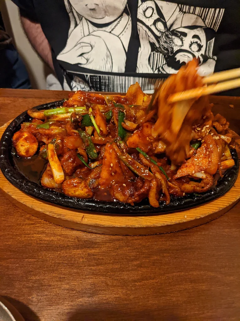 Spicy squid and vegetable stir-fry on a cast-iron plate, chopsticks lifting a piece from the pile