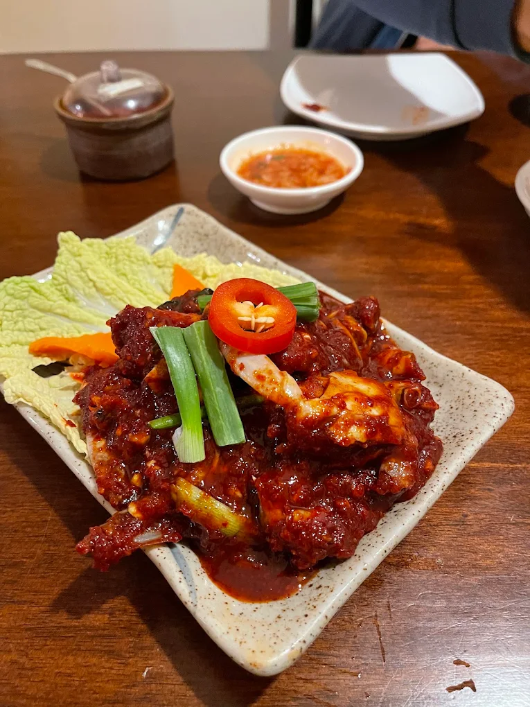 Spicy marinated crab in red chilli sauce on a ceramic plate, topped with scallion and fresh chilli