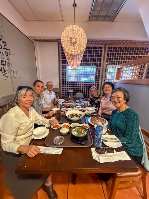 A group of friends gathered around a shared table of Korean dishes at Jang Dok Dae