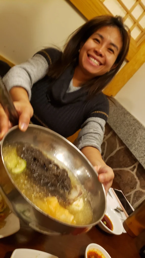 A smiling guest holding up a large bowl of Korean soup at Jang Dok Dae